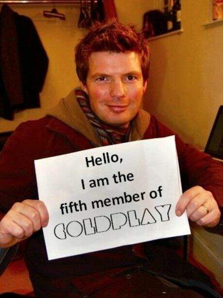 Empresário Phil Harvey com a placa "Olá, eu sou o quinto membro do Coldplay"